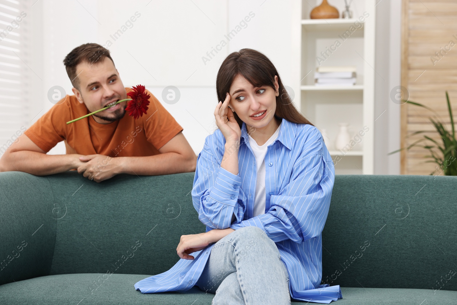 Photo of Man with flower in mouth flirting with embarrassed woman at home