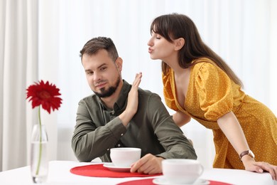 Bad date. Embarrassed man refusing from woman's kiss indoors