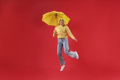 Photo of Woman with yellow umbrella jumping on red background