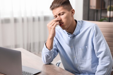 Photo of Young man suffering from sinusitis at wooden table indoors