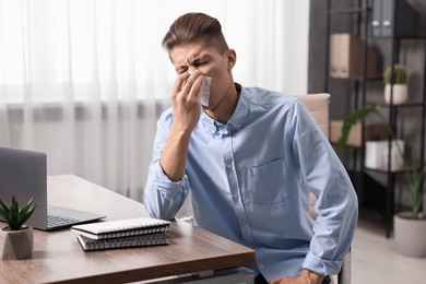 Young man with tissue suffering from sinusitis at wooden table indoors