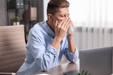 Young man with tissue suffering from sinusitis at wooden table indoors