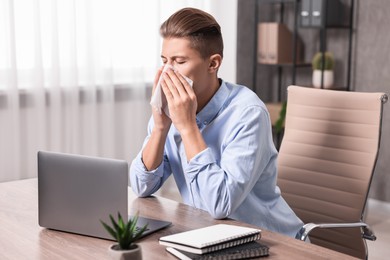 Photo of Young man with tissue suffering from sinusitis at wooden table indoors