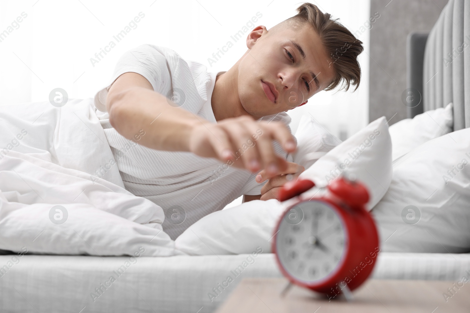 Photo of Sleepy young man turning off alarm clock in bedroom at lunch time