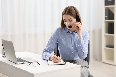 Teenager in headset taking notes while working at table indoors. Remote job