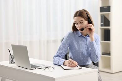 Teenager in headset taking notes while working at table indoors. Remote job