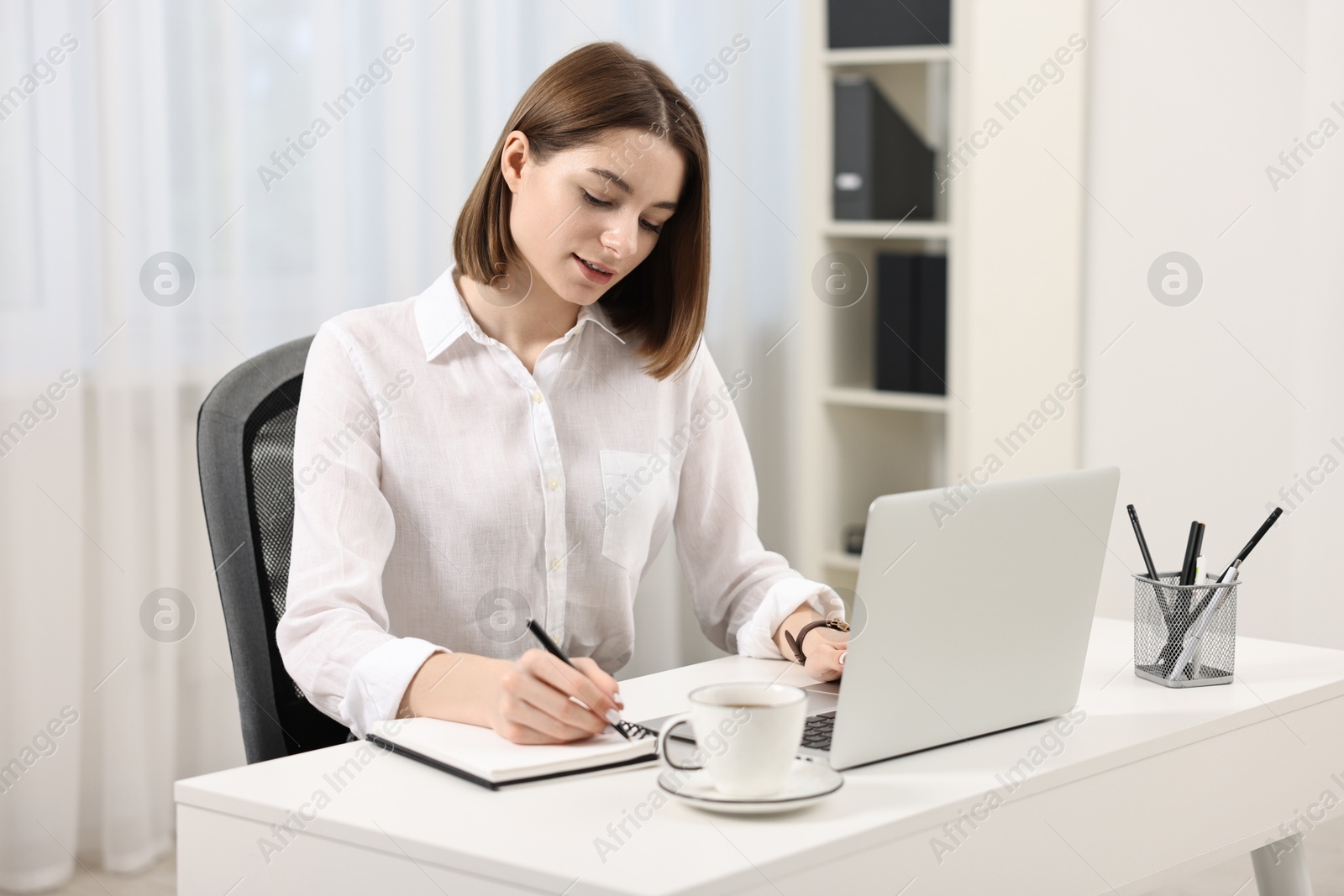 Photo of Teenager taking notes while working with laptop at home. Remote job