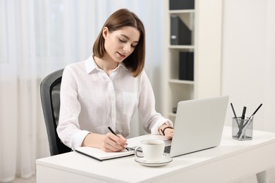 Teenager taking notes while working with laptop at home. Remote job