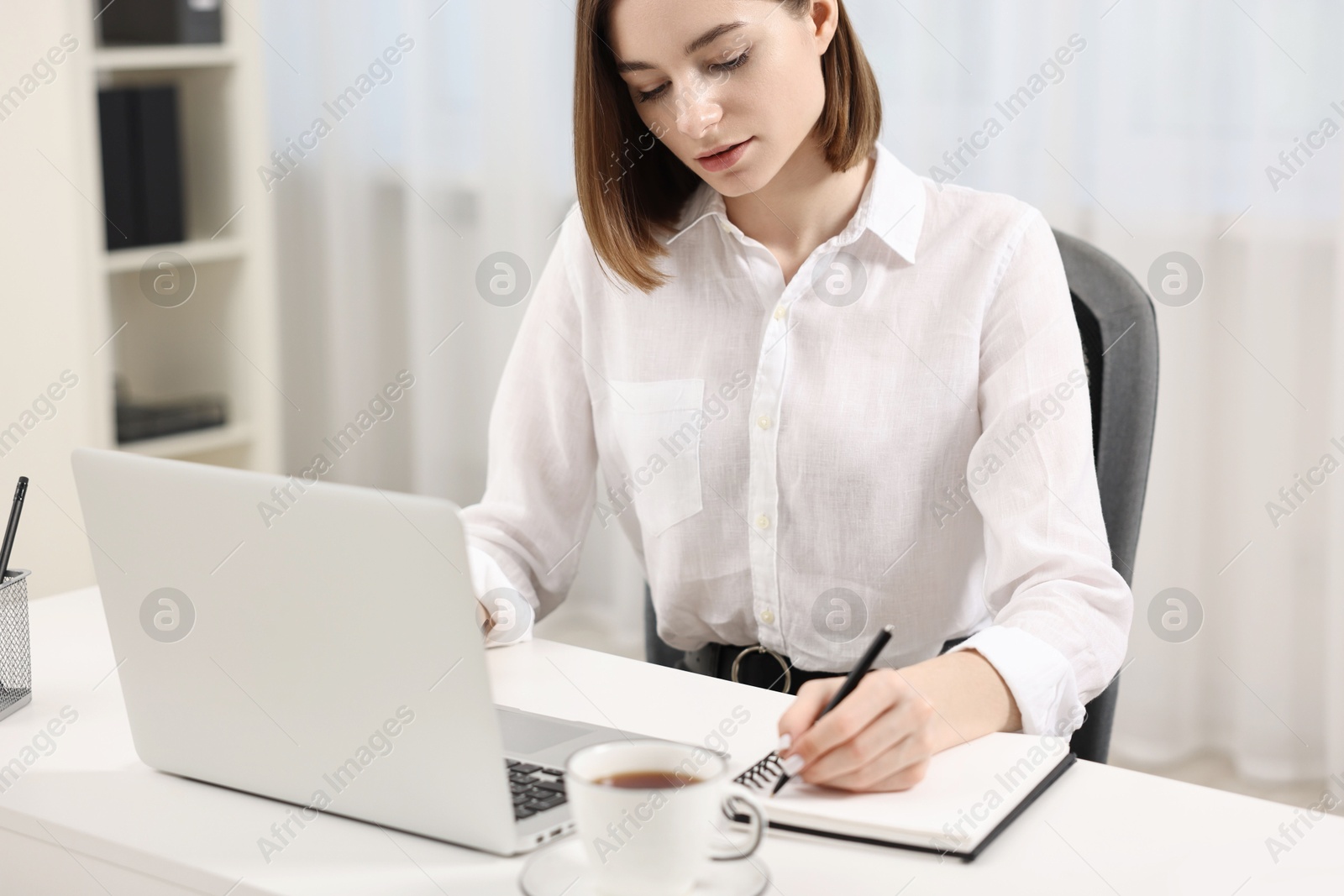 Photo of Teenager taking notes while working with laptop at home. Remote job