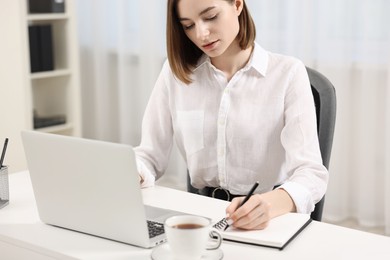 Teenager taking notes while working with laptop at home. Remote job