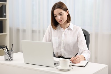 Teenager taking notes while working with laptop at home. Remote job