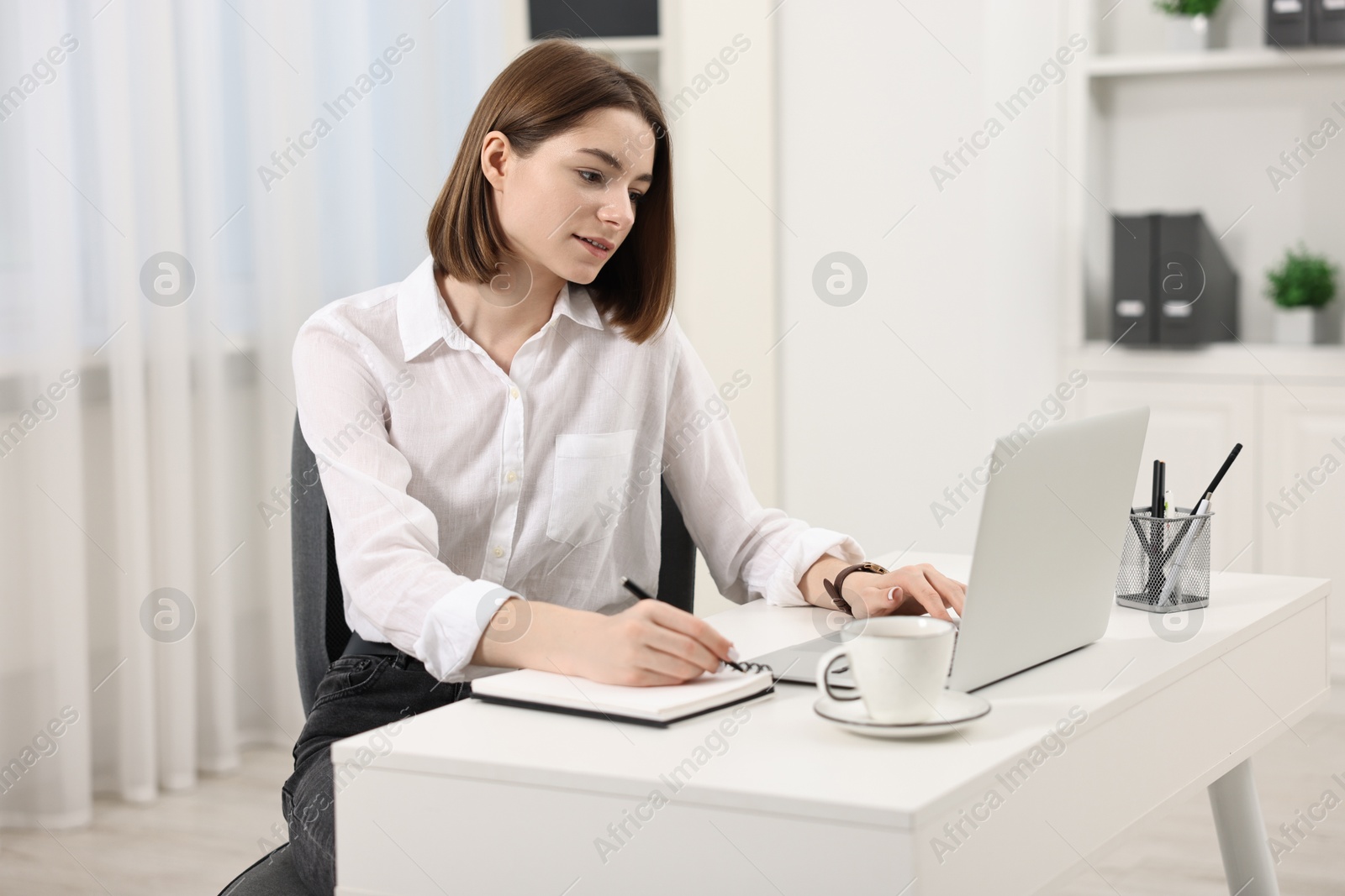 Photo of Teenager taking notes while working with laptop at home. Remote job