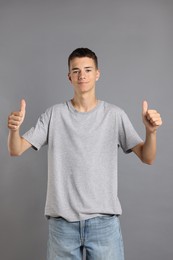 Photo of Teenage boy wearing t-shirt and showing thumbs up on grey background