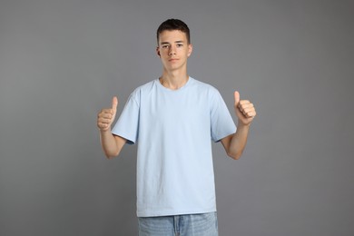 Teenage boy wearing light blue t-shirt and showing thumbs up on grey background