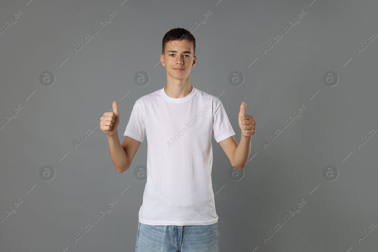 Photo of Teenage boy wearing white t-shirt and showing thumbs up on grey background