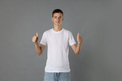 Teenage boy wearing white t-shirt and showing thumbs up on grey background