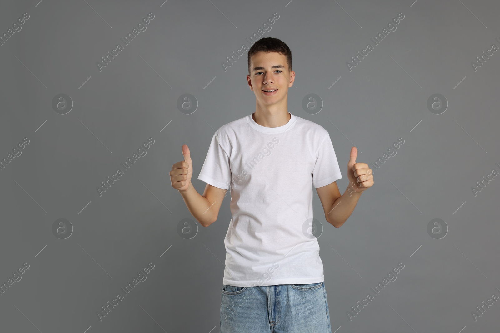 Photo of Teenage boy wearing white t-shirt and showing thumbs up on grey background