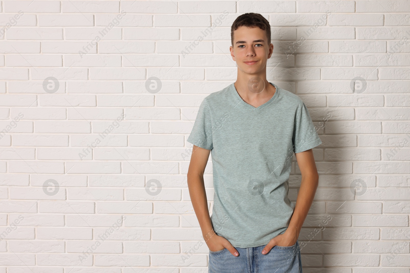 Photo of Teenage boy wearing grey t-shirt near white brick wall, space for text