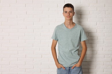 Teenage boy wearing grey t-shirt near white brick wall, space for text