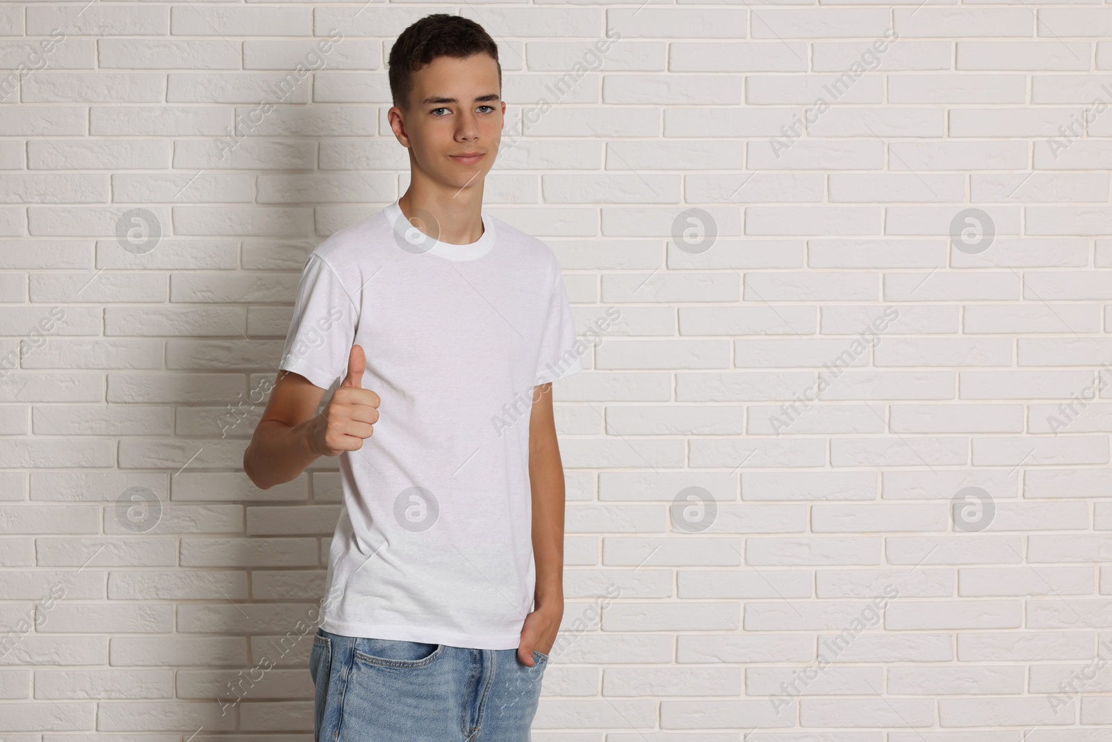 Photo of Teenage boy wearing t-shirt near white brick wall, space for text