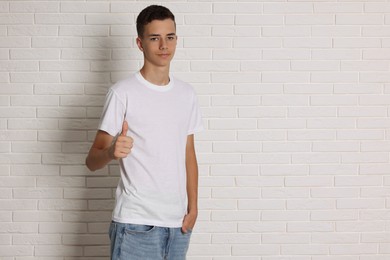 Teenage boy wearing t-shirt near white brick wall, space for text