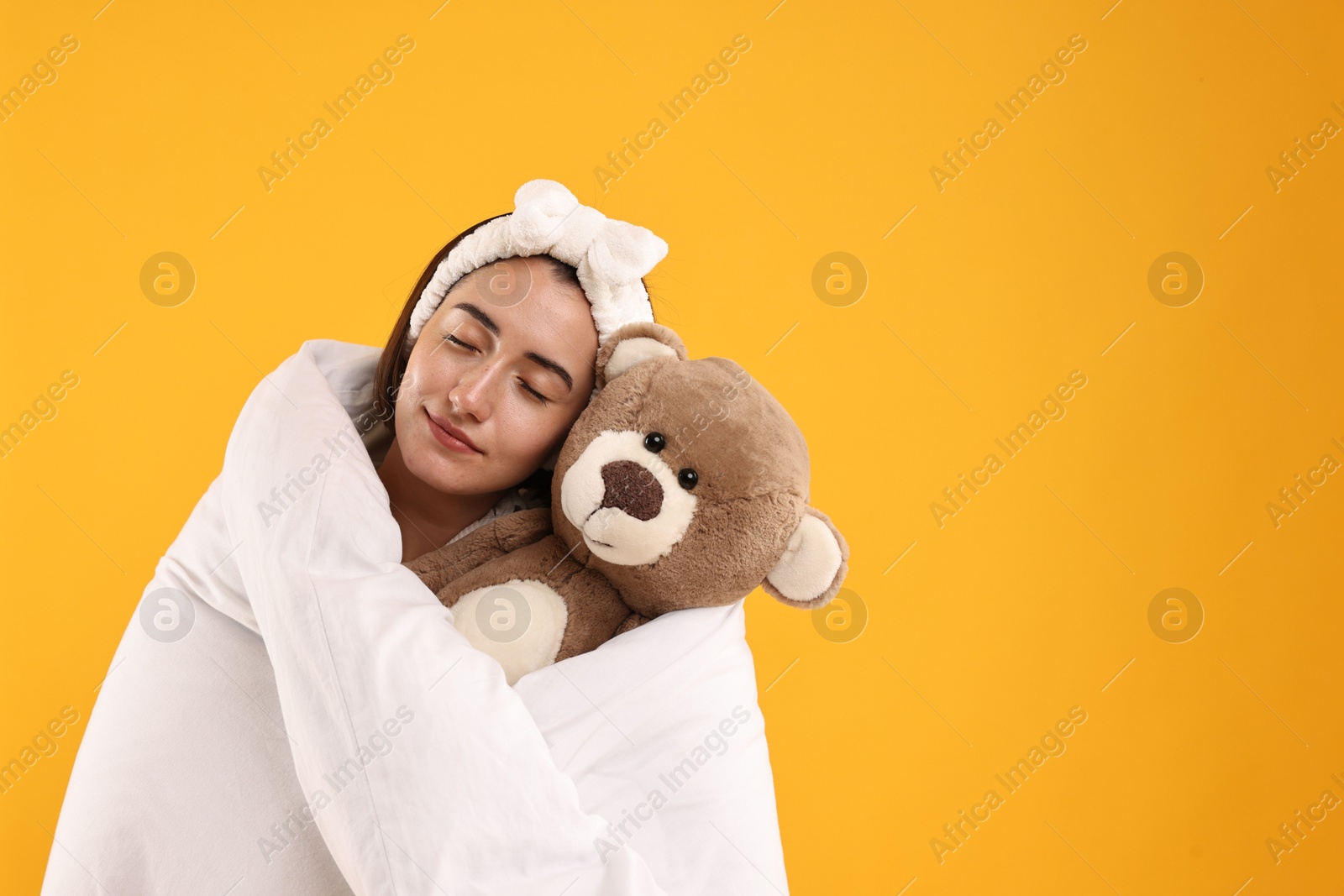 Photo of Happy young woman with teddy bear wrapped in blanket on yellow background. Space for text