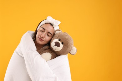 Happy young woman with teddy bear wrapped in blanket on yellow background. Space for text