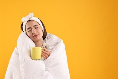 Happy young woman with cup wrapped in blanket on yellow background. Space for text