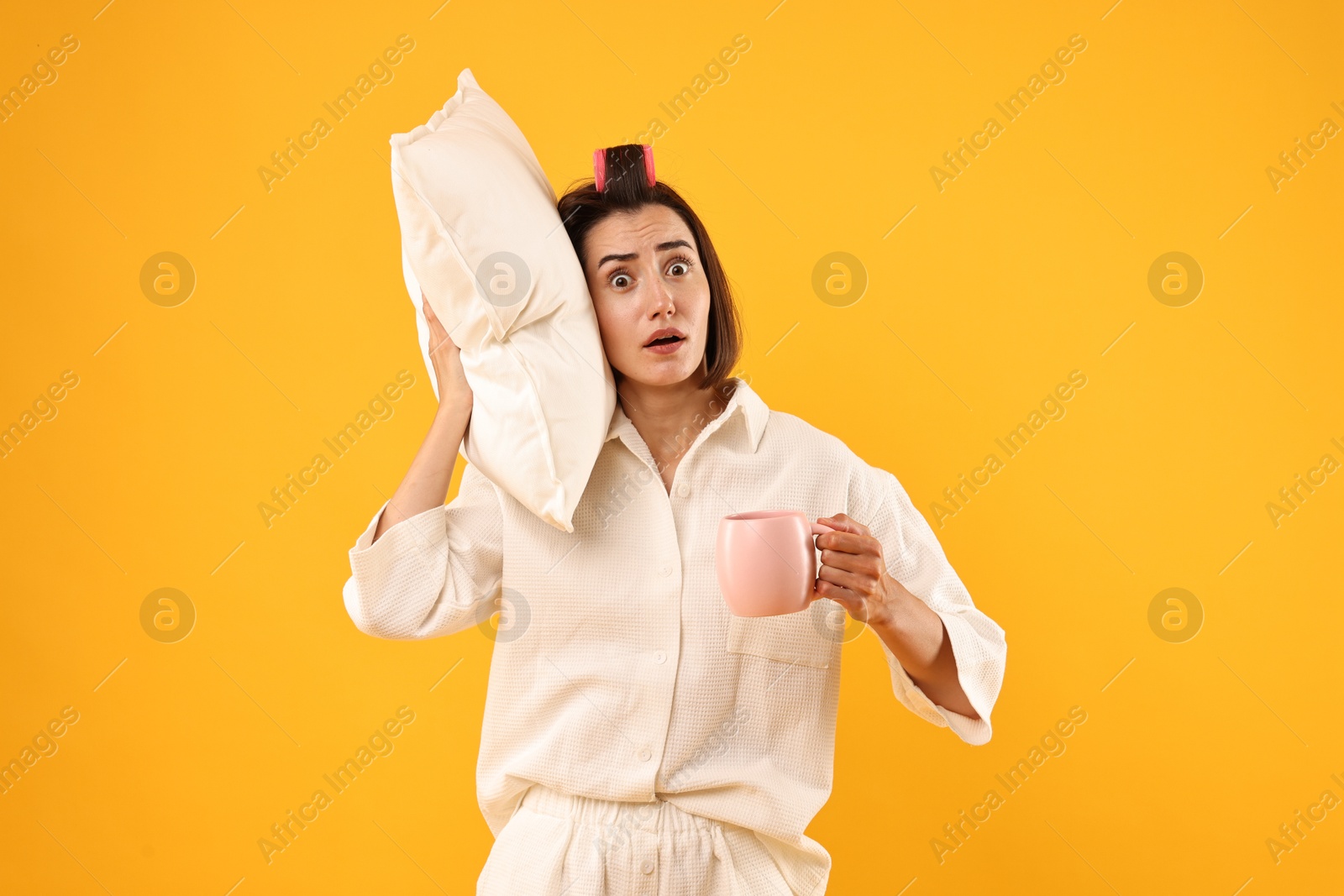 Photo of Overslept young woman with pillow and cup on yellow background