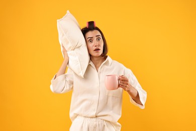 Overslept young woman with pillow and cup on yellow background