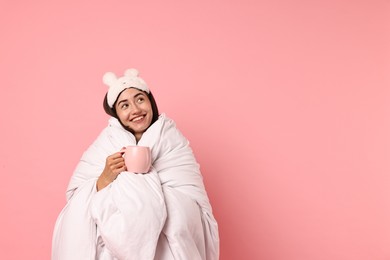 Photo of Happy young woman with cup wrapped in blanket on pink background. Space for text