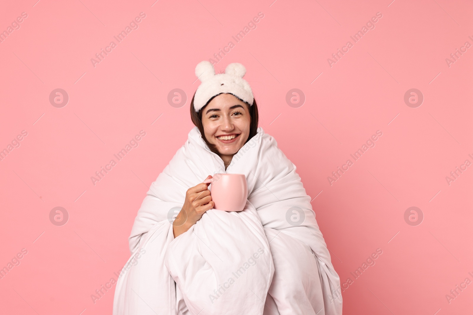 Photo of Happy young woman with cup wrapped in blanket on pink background