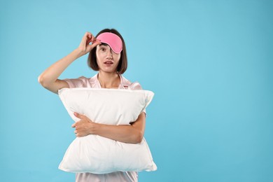 Photo of Overslept young woman with sleep mask and pillow on light blue background. Space for text