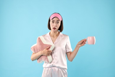 Overslept young woman with sleep mask, cup and pillow on light blue background