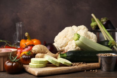 Photo of Cooking tasty stew. Fresh zucchini, ginger, tomatoes, cauliflower and peppercorns on wooden table