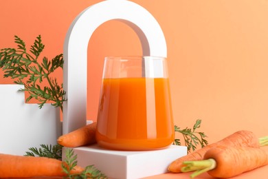 Fresh carrot juice in glass and vegetables on coral background, closeup