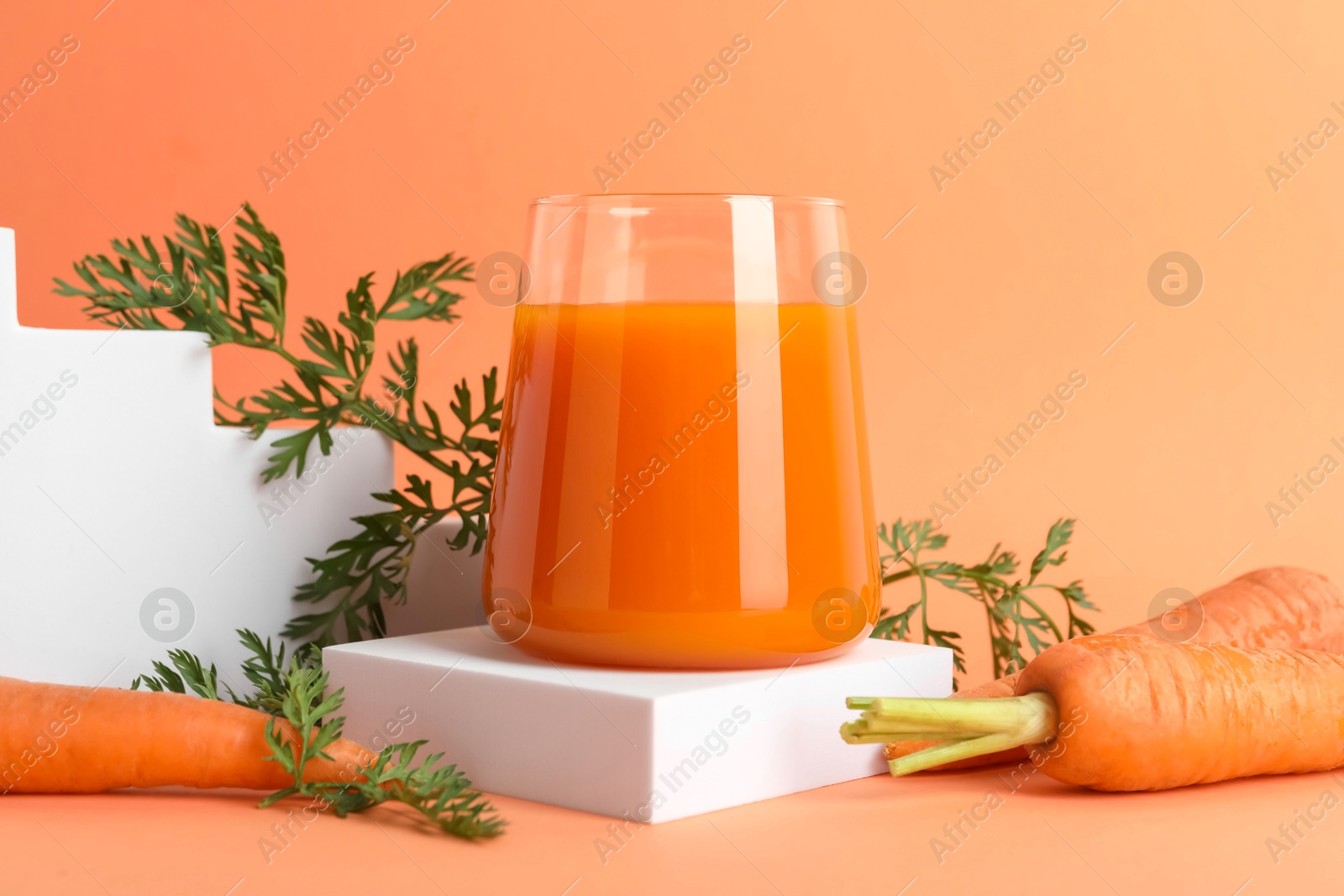 Photo of Fresh carrot juice in glass and vegetables on coral background, closeup