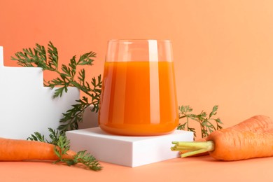 Fresh carrot juice in glass and vegetables on coral background, closeup