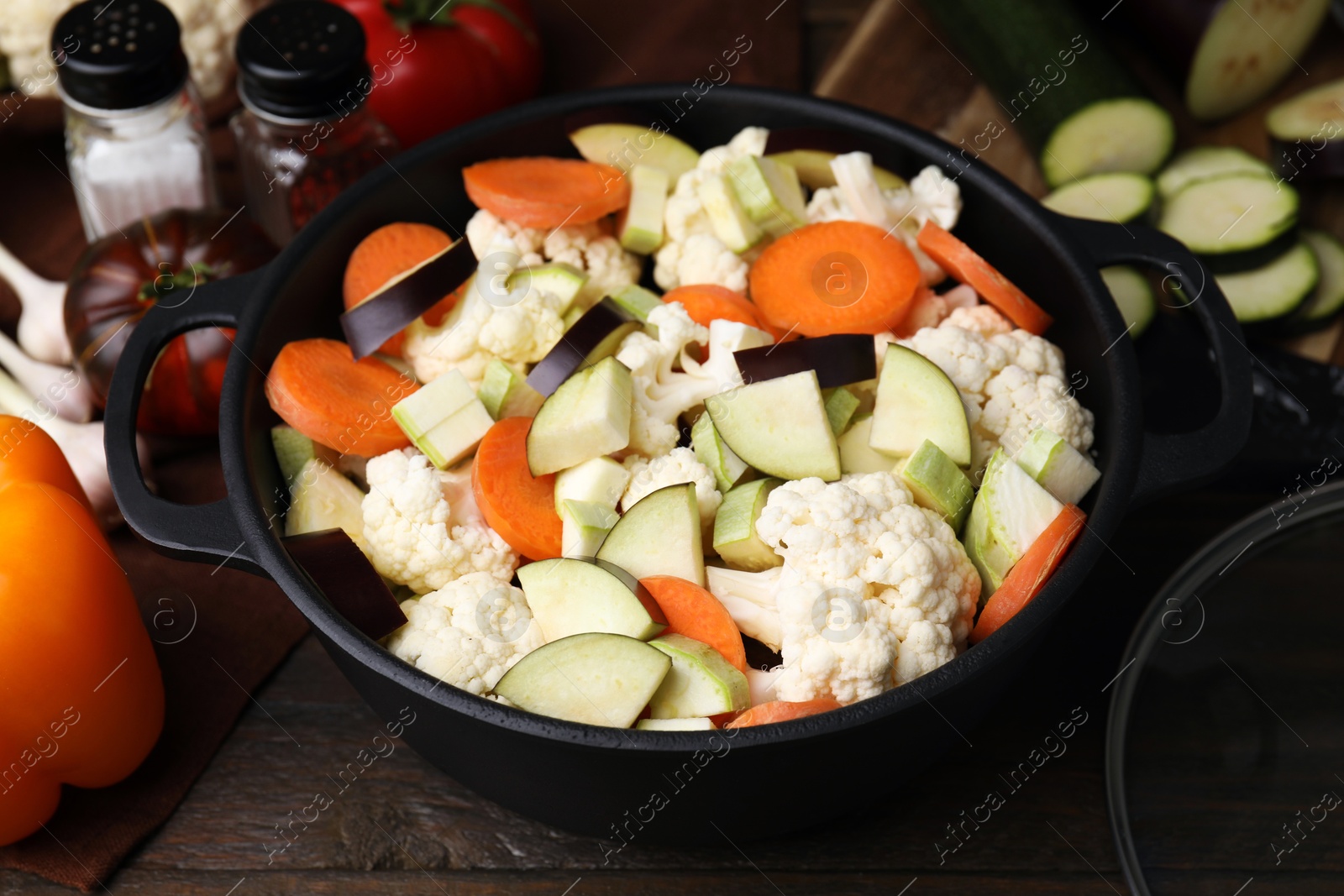 Photo of Cooking stew. Cut raw vegetables in pot on wooden table, closeup