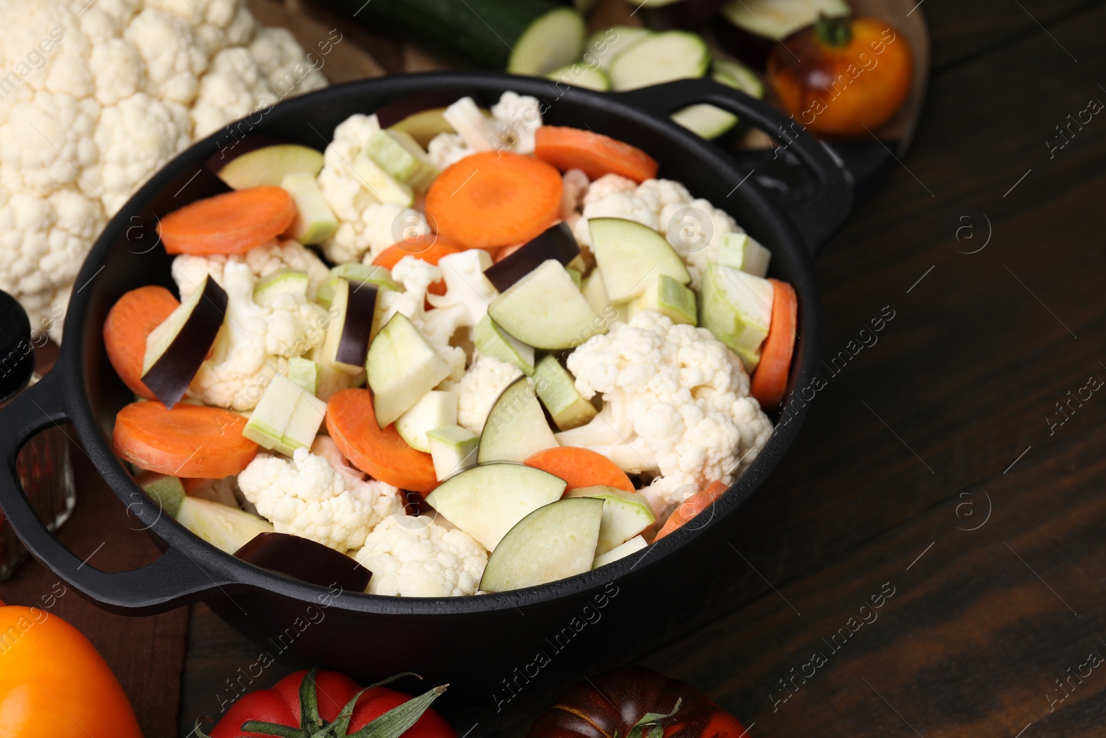 Photo of Cooking stew. Cut raw vegetables in pot on wooden table, closeup