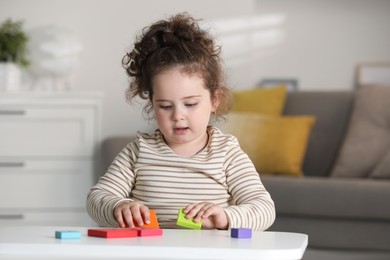 Photo of Portrait of cute girl playing with wooden geometric figures at table indoors. Adorable child