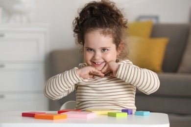 Portrait of smiling girl playing with wooden geometric figures at table indoors. Adorable child