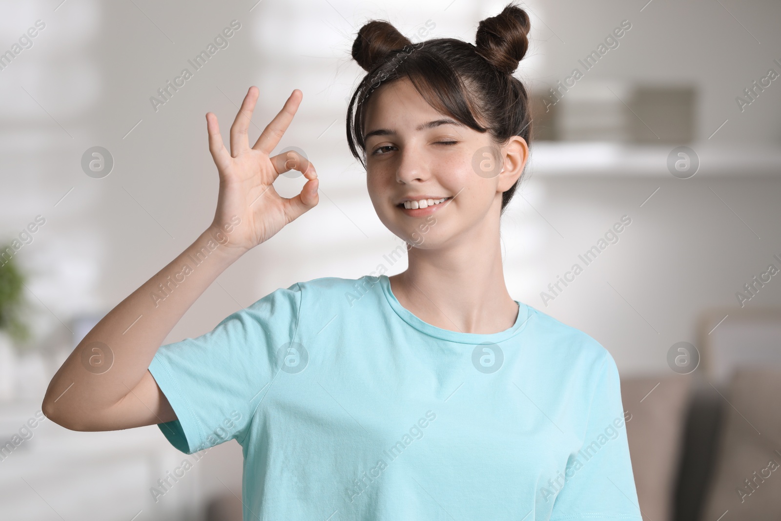 Photo of Portrait of smiling teenage girl showing ok gesture at home