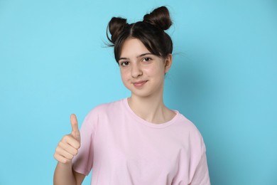 Photo of Portrait of teenage girl showing thumbs up on light blue background