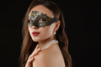 Beautiful woman wearing carnival mask on black background, closeup