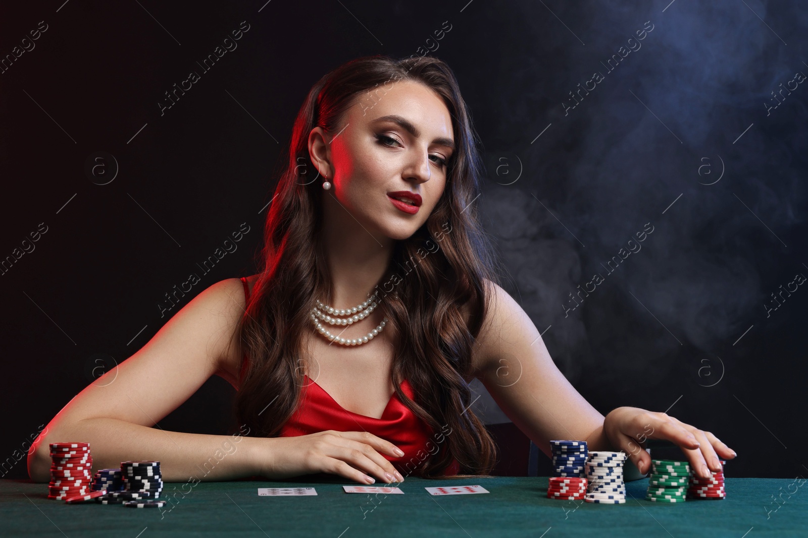 Photo of Charming woman playing poker at table on black background with smoke