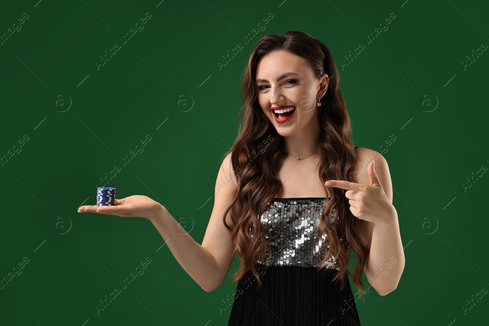 Photo of Happy woman pointing at poker chips on green background