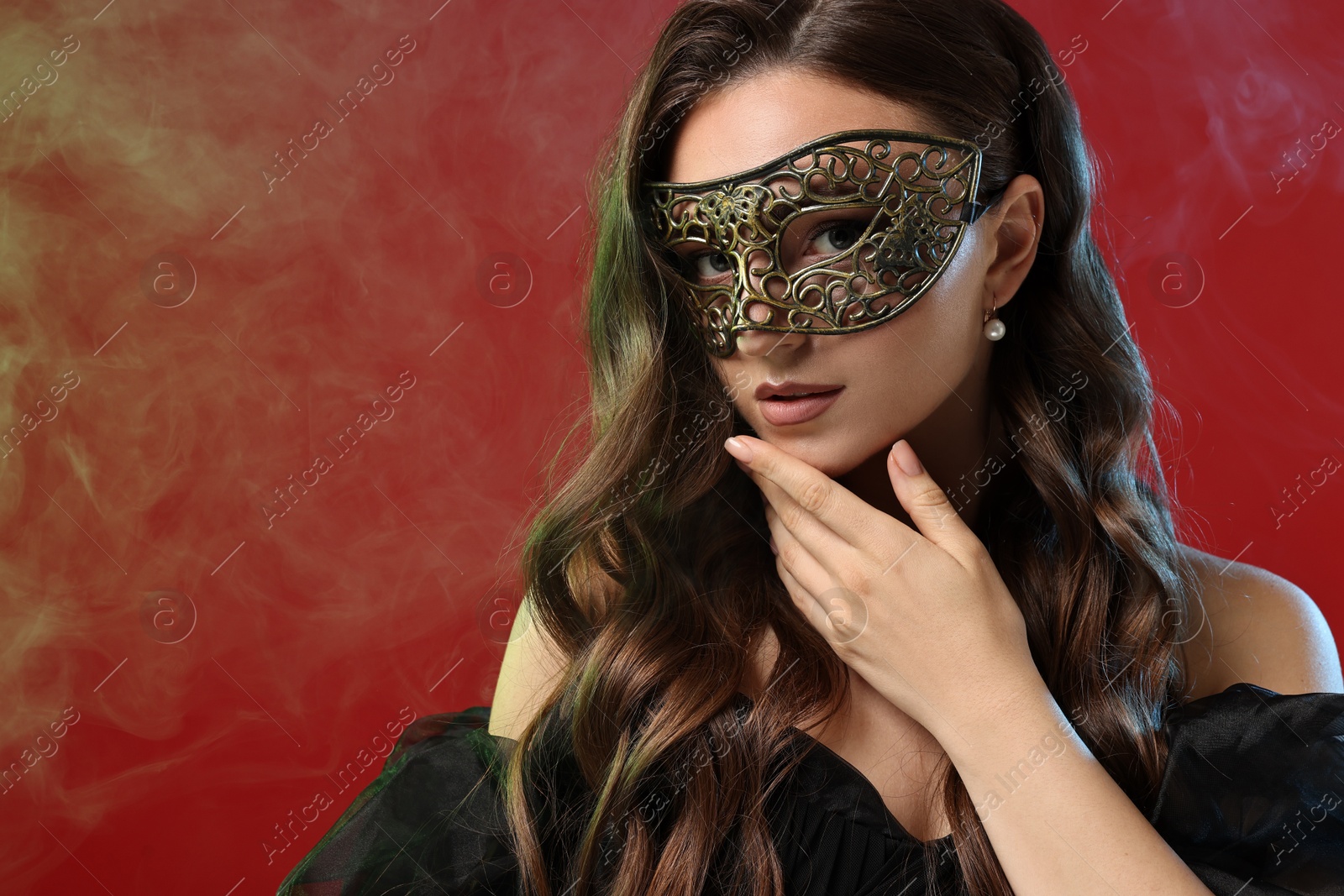 Photo of Beautiful woman wearing carnival mask on red background in color lights and smoke. Space for text