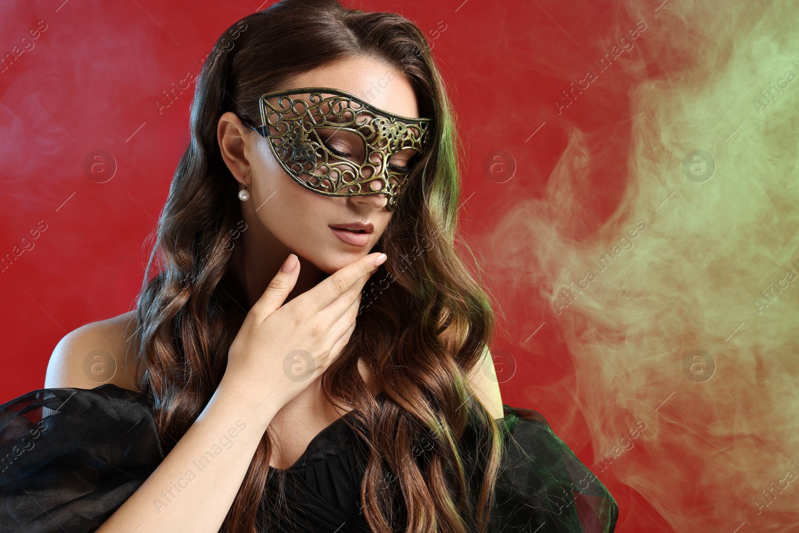 Photo of Beautiful woman wearing carnival mask on red background in color lights and smoke. Space for text