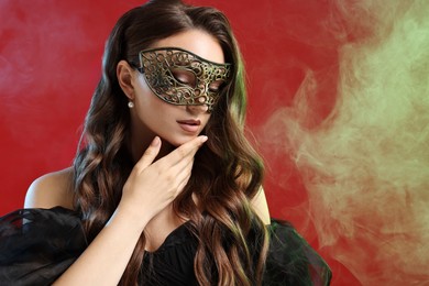 Photo of Beautiful woman wearing carnival mask on red background in color lights and smoke. Space for text